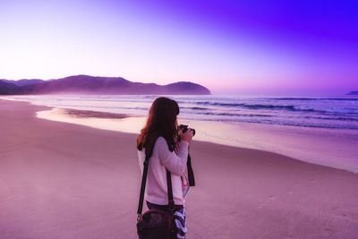 Woman photographing sea against sky during sunrise
