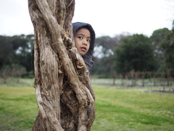 Portrait of boy hiding behind tree trunk at park