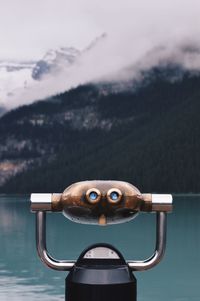 Coin-operated binoculars by lake against mountain
