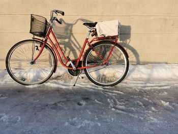 A red bicycle leaning against light colored wall with horizontal lines, a white parcel on the rack