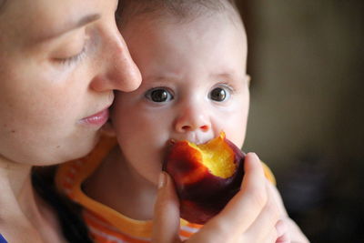 Close-up mother feeding daughter plum at home