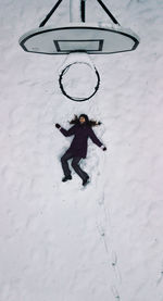 High angle view of young woman lying on snow by basketball hoop