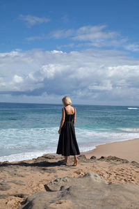 Rear view of woman standing at beach against sky