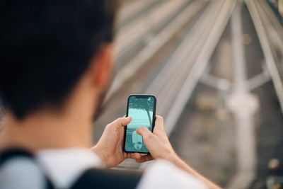 Cropped image of young man using smart phone over railroad tracks in city