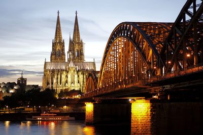 Cologne cathedral and illuminated hohenzollern bridge against sky during sunset