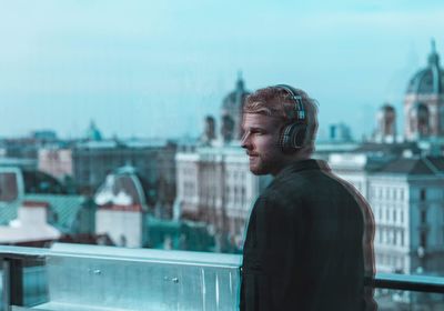 Side view of young man looking away against buildings in city