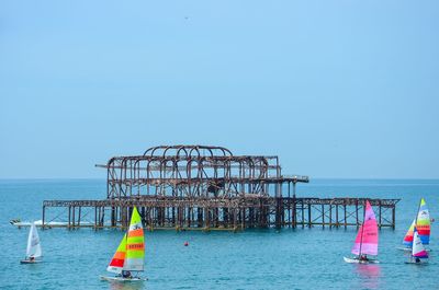 Pier in sea with sailboats against clear sky