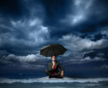 Full length of man with umbrella on sea during sunset