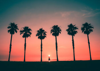 Silhouette person standing amidst palm trees against sky during sunset