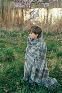 Portrait of a little boy wrapped in a blanket enjoying cherry blossoms in a city park.