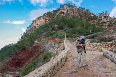 Full length of man carrying son while standing on pathway against mountain