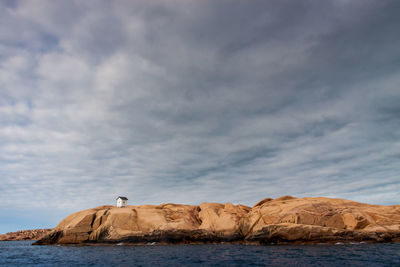 Mid distant view of hut on rock formation at sea shore against sky