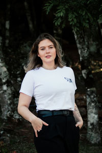 Portrait of beautiful young woman standing against trees