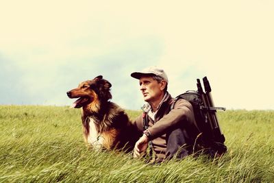 Man with dog sitting on field against sky