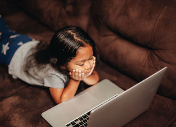 Cute girl using laptop while lying on sofa at home