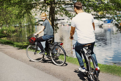 Happy businesswoman looking at colleague while riding bicycles on street by lake