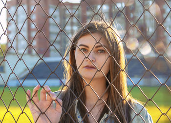 Portrait of young woman looking through fence outdoors
