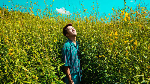 Young man with eyes closed standing by plants during sunny day