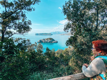 Rear view of woman sitting by sea against sky