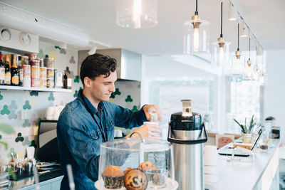 Young owner making coffee at checkout counter in office cafe