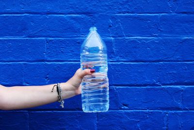 Close-up of hand holding bottle against blue wall
