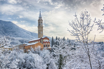 Low angle view of church amidst trees against cloudy sky during winter