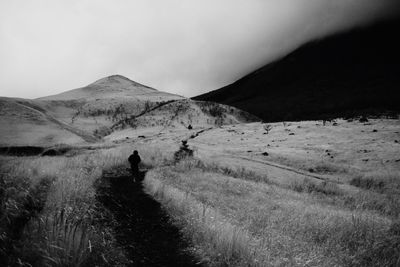 Man walking on road by mountain against sky