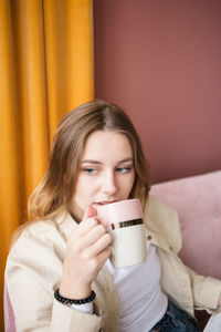 Young woman close-up drinks tea, coffee in ceramic cup in living room