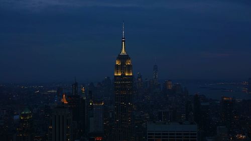 Illuminated empire state building by cityscape against sky at night