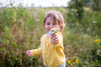 Girl holding yellow flowers on field