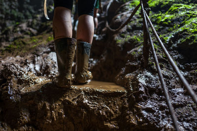 Low section of woman wearing muddy rubber boots while standing on rock in forest