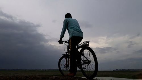 Rear view of man riding bicycle on field against sky