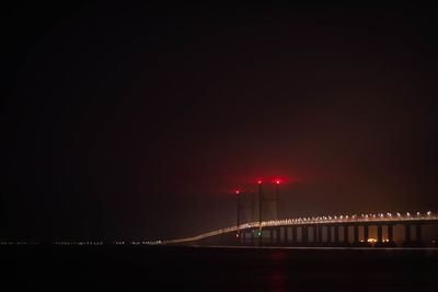 Illuminated bridge over sea against sky at night