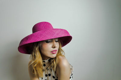 Close-up of beautiful young woman wearing hat against wall