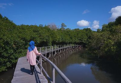 Rear view of woman standing on footbridge over river