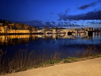 Illuminated buildings by lake against sky at night