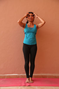 Full length of woman performing yoga while standing against orange wall