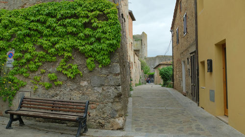 Empty bench amidst buildings against sky