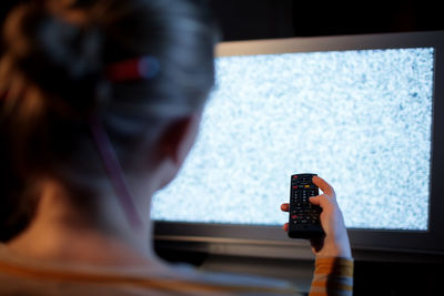 Rear view of woman changing television set channels at home