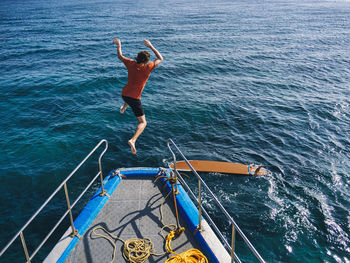 Adventurous man jumping off from boat deck for surfing on sunny day