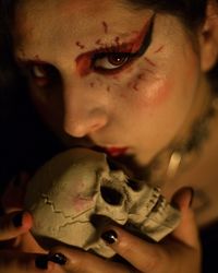 Portrait of young woman with make-up kissing skull