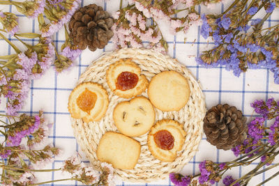 Flat lay of sweets, butter cookie on rattan plate in center of statice flower on blue gingham cloth.