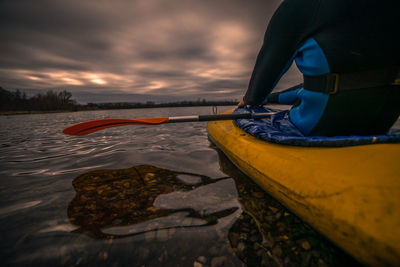 Midsection of man kayaking in lake against sky during sunset