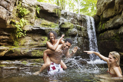 Cheerful friends laughing and splashing in river by waterfall