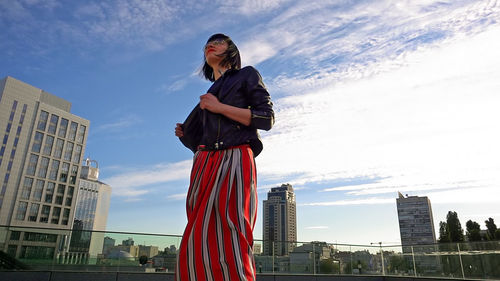 Happy woman wearing striped skirt and jacket on footpath in city