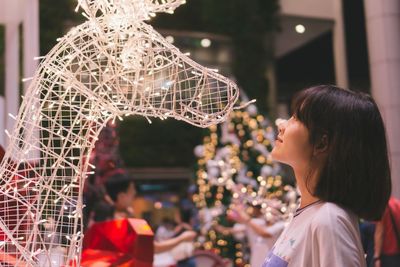 Side view of smiling girl looking at illuminated christmas decoration at home
