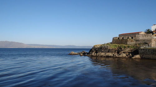 Scenic view of sea by buildings against clear blue sky