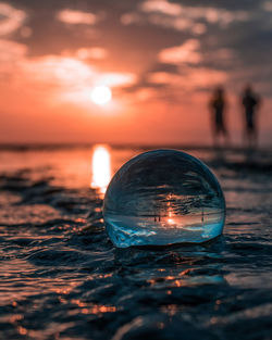 Close-up of crystal ball in sea against sunset sky