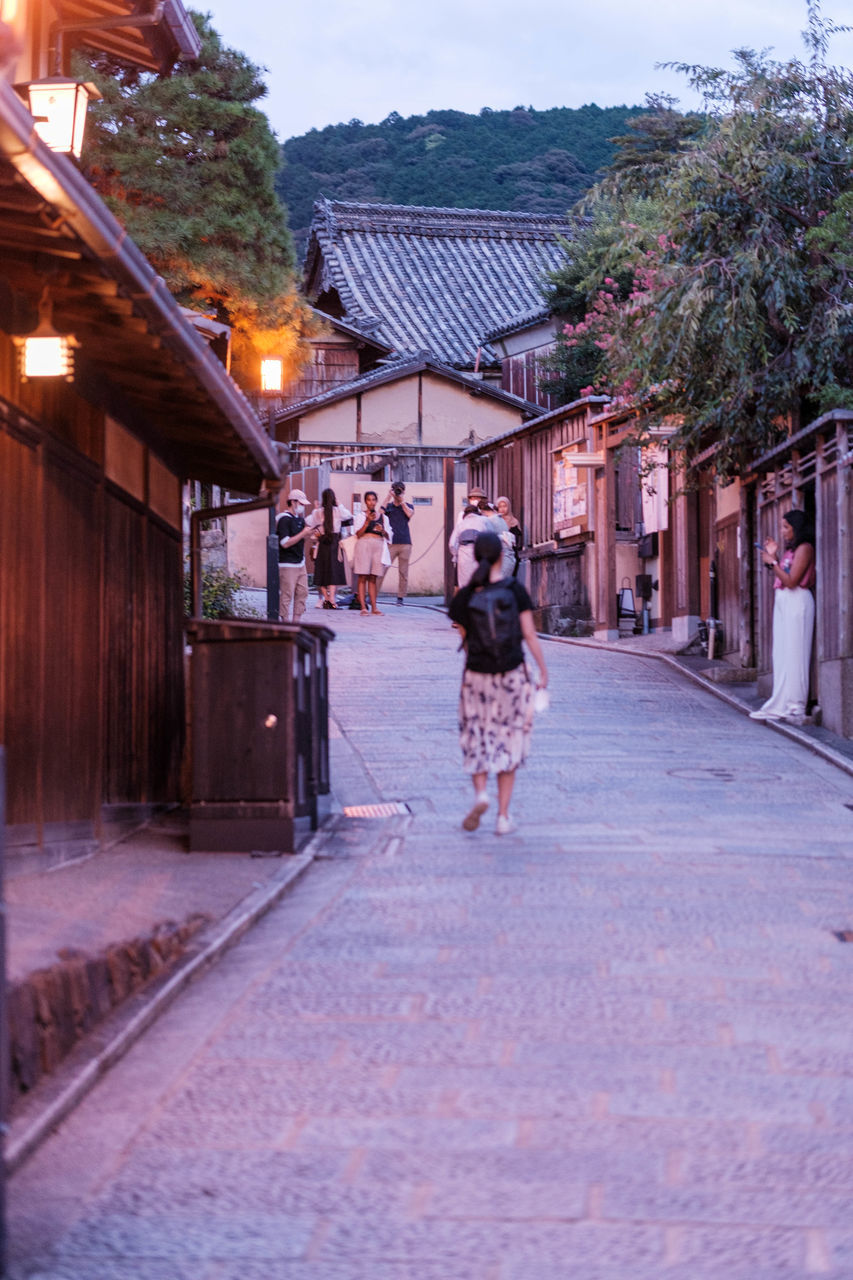 architecture, building exterior, built structure, city, adult, town, street, walking, building, full length, women, one person, nature, road, rear view, lifestyles, house, sky, person, residential district, outdoors, footpath, clothing, footwear, travel, urban area, travel destinations, tree, motion, plant