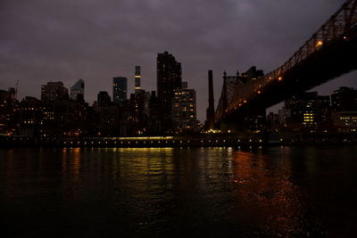 Illuminated buildings by river against sky at night